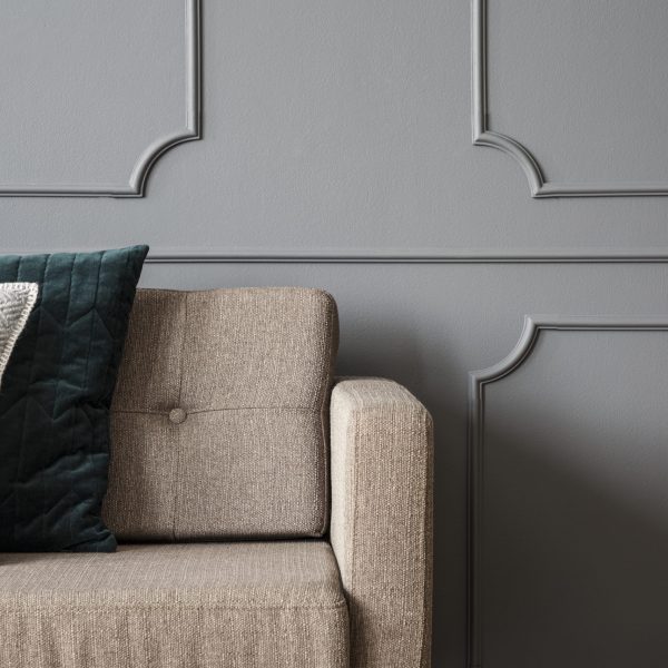 Close-up of pillows on beige sofa against grey wall with molding in living room interior. Real photo