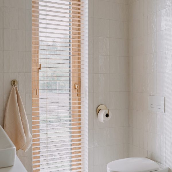 A modern bathroom with white tiled walls and wood accents, featuring a toilet and a window