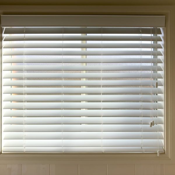 White wooden window blinds partially open with adjustment cords inside a house