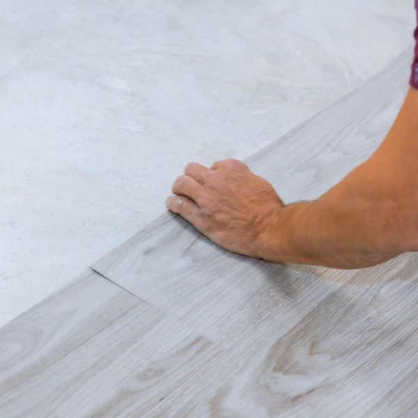 Work on laying worker installing new vinyl tile laminate wood texture floor.