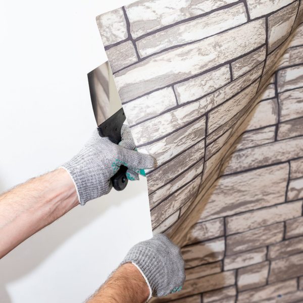 woman tears off Wallpaper, removing Wallpaper from the wall with a spatula, the process of updating the wall room repair.